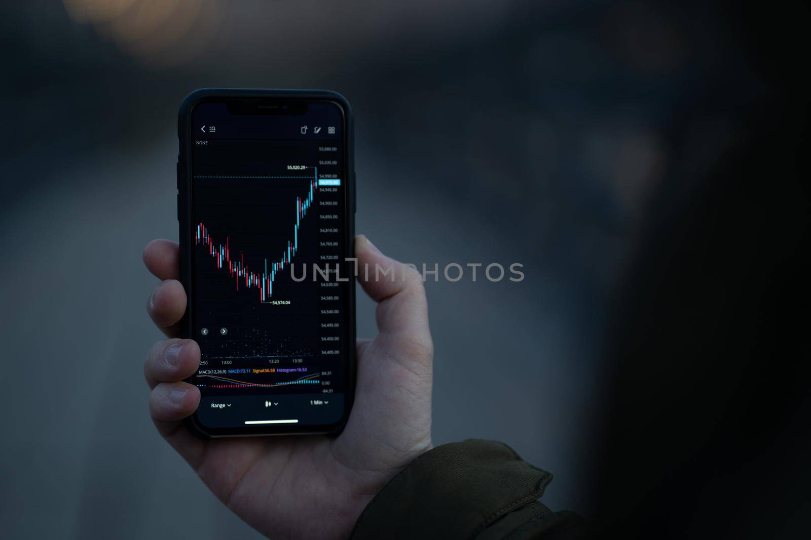 Forex trading. Male hand holding smartphone with candlestick chart on screen, trader reading financial news and checking real time foreign exchange market data in mobile app while stnading outdoors