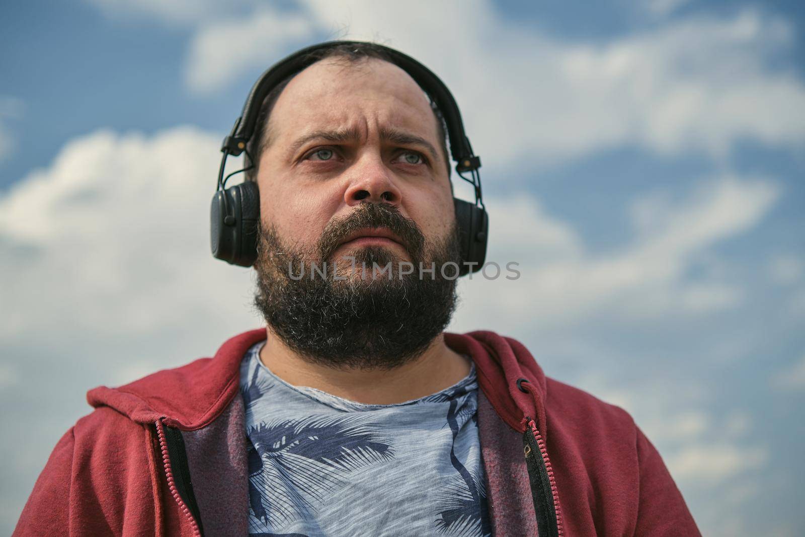 Middle-aged European man in headphones outdoors listening to music against the background of the sky