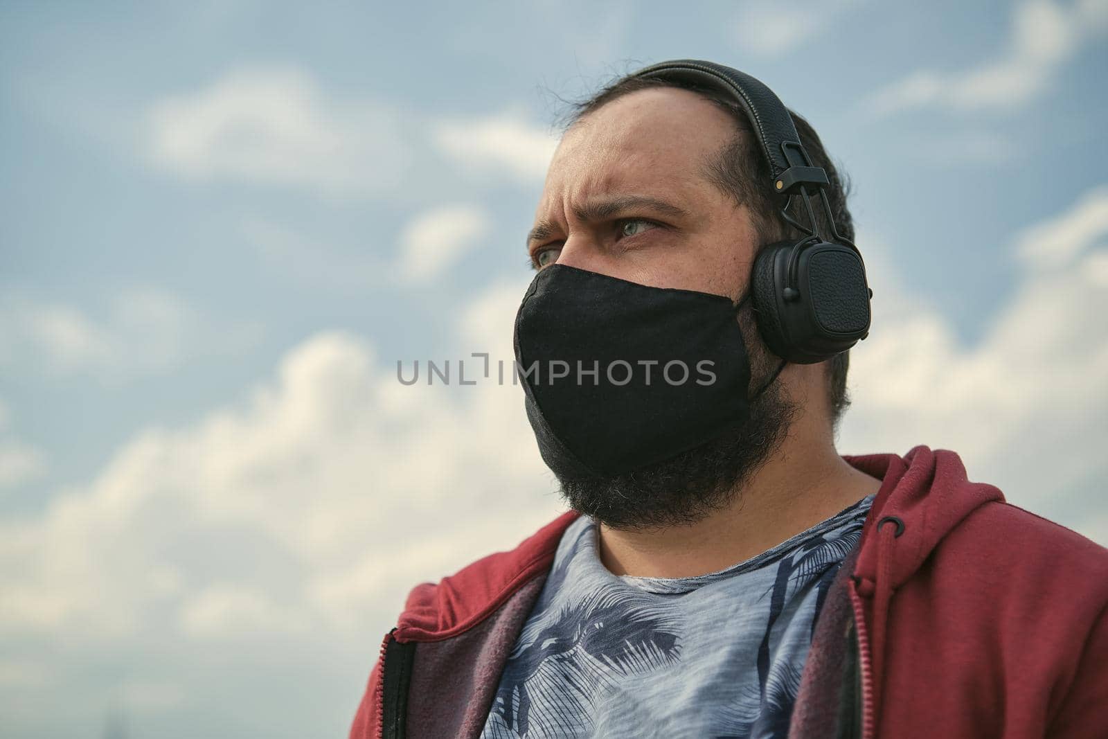 Middle-aged European man in headphones outdoors listening to music against the background of the sky