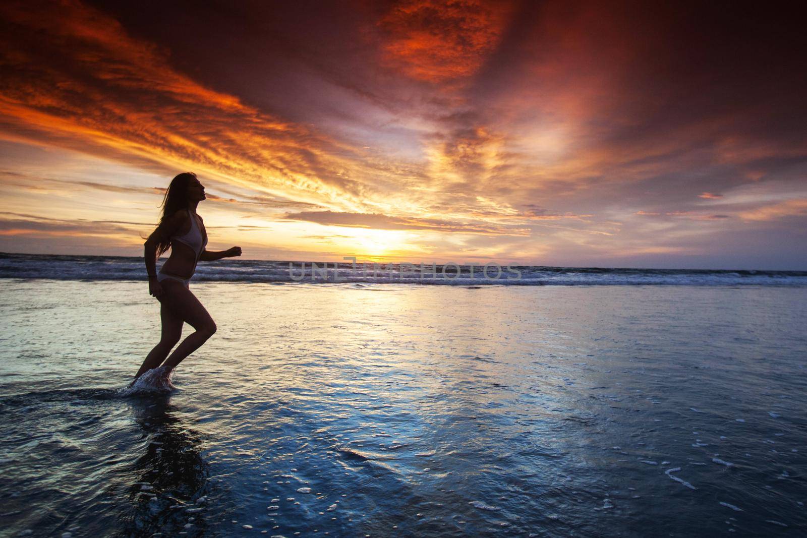 Woman running by the ocean beach at sunset