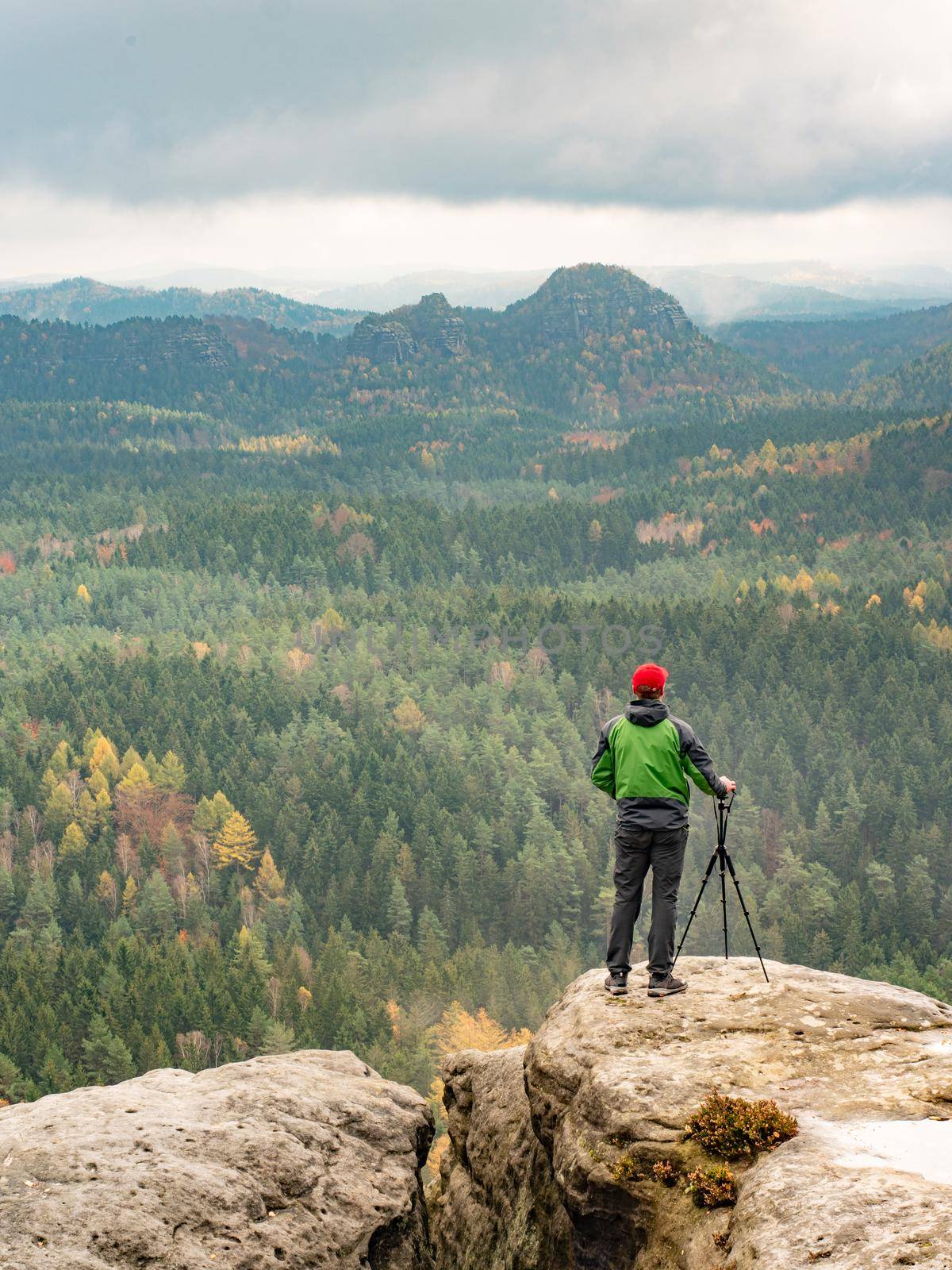 Travel hobby photographer taking picture of misty mountain landscape using professional camera on tripod on stormy, autumn day