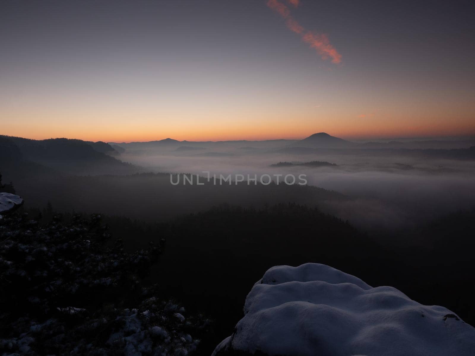 Chill morning with snow on rocky edge, valley full colorful mist. Winter hilly landscape 