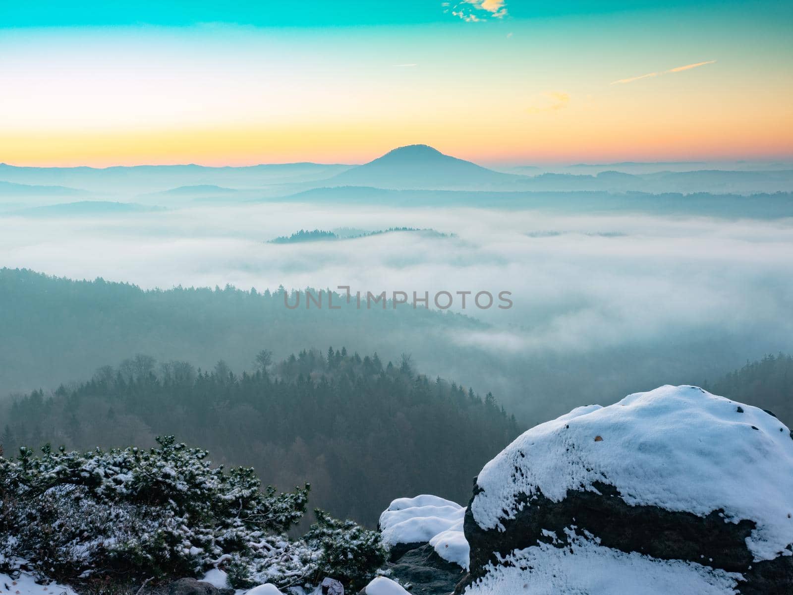 Mountain morning  landscape with fog and trees. Snowy rocks in foreground