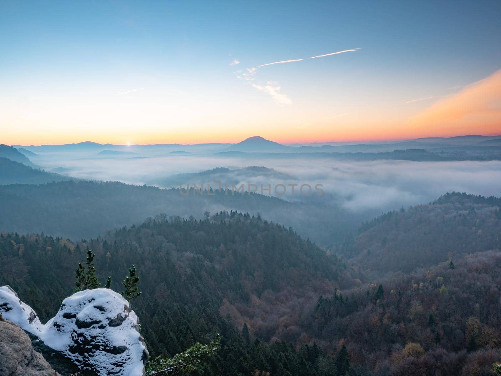 Chill morning with snow on rocky edge, valley full colorful mist. Winter hilly landscape 