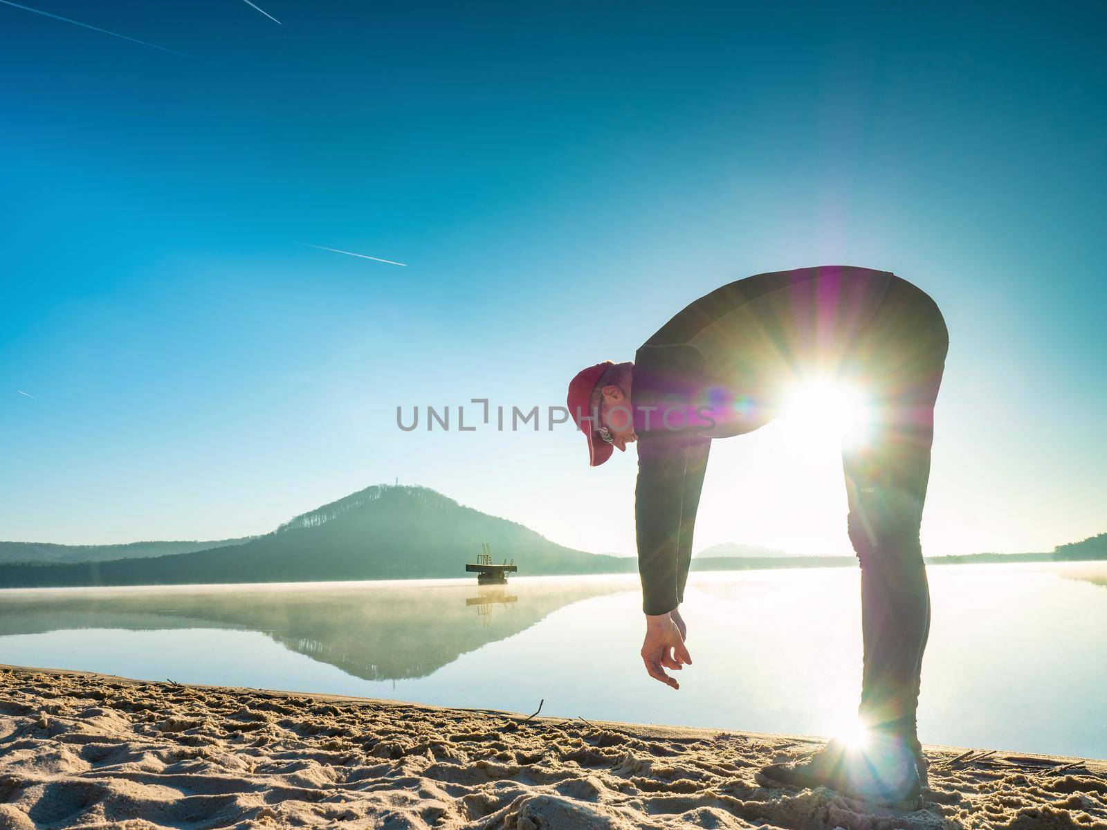 Young sporty fitoman doing stretching body and do yoga  on beach. Sunny morning