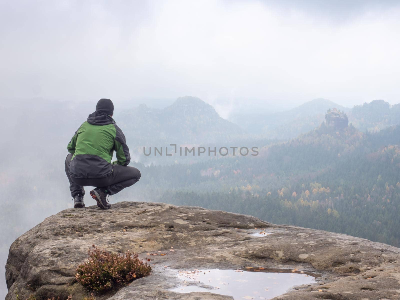 Man sitting at the peak of mountain on foggy morning.  Sit squatting at edge by rdonar2