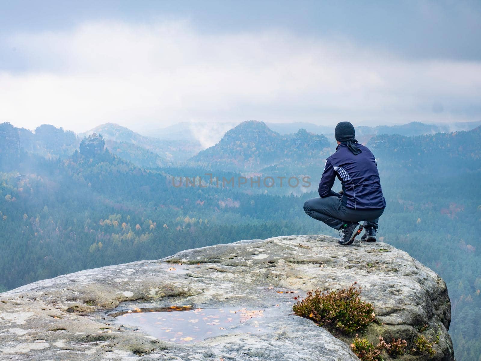 Man sitting at the peak of a mountain on a foggy morning.  Sit squatting on the peak edge and enjoying mountains view valley during heavy mist