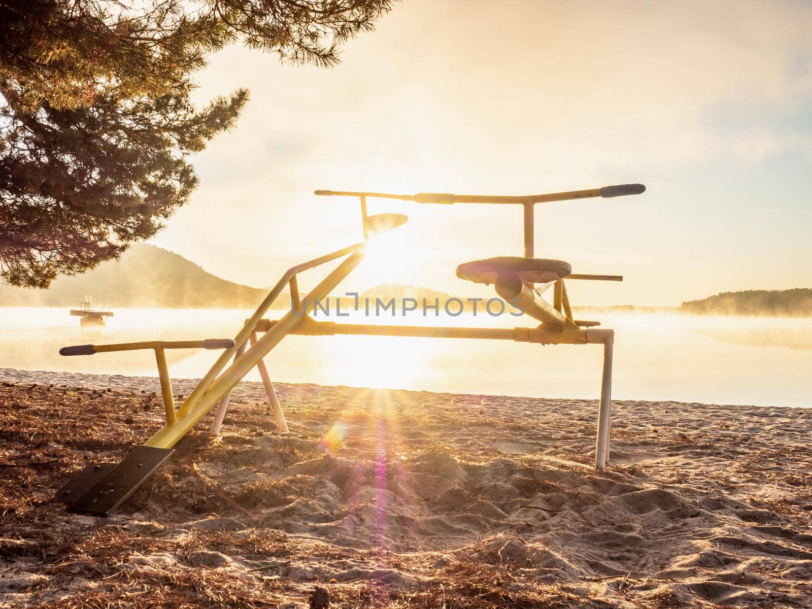 Colorful sunset with seesaw on beach. Teeter totter with wooden chairs,  sand balance close up outdoor playground