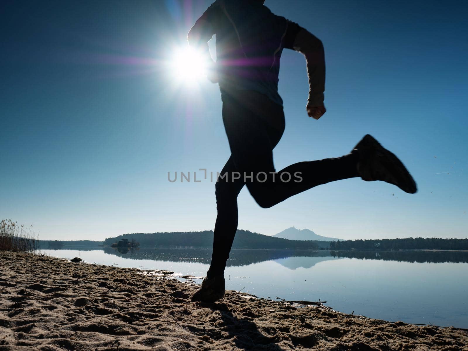 Silhouette young sport man running outdoors on beach at sunset with orange sky