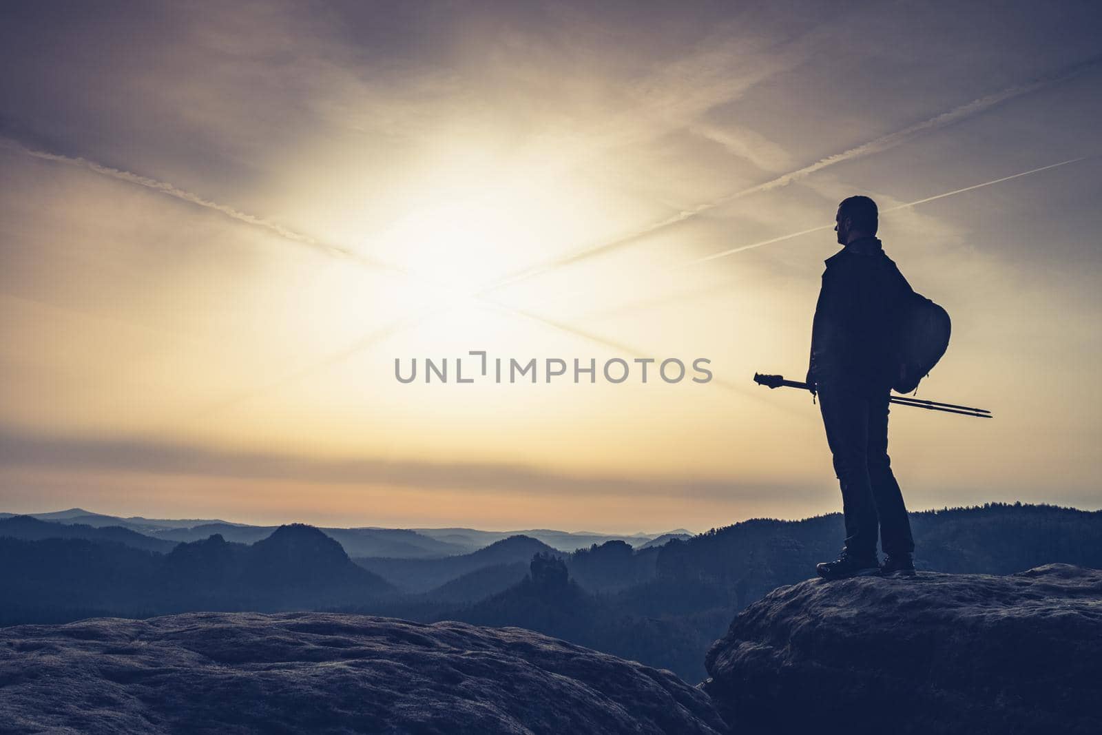 Silhouette of hiker with backpack and walking poles is going in mountains and sunset 