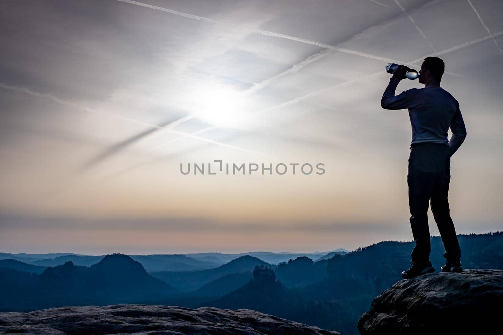 Handsome traveler with bottle drinking water within summer trip  in rocks