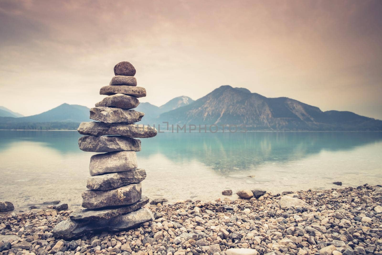 Hobby of rock stacking at Alps lake beach. Balanced stones on a pebble beach during sunset. 