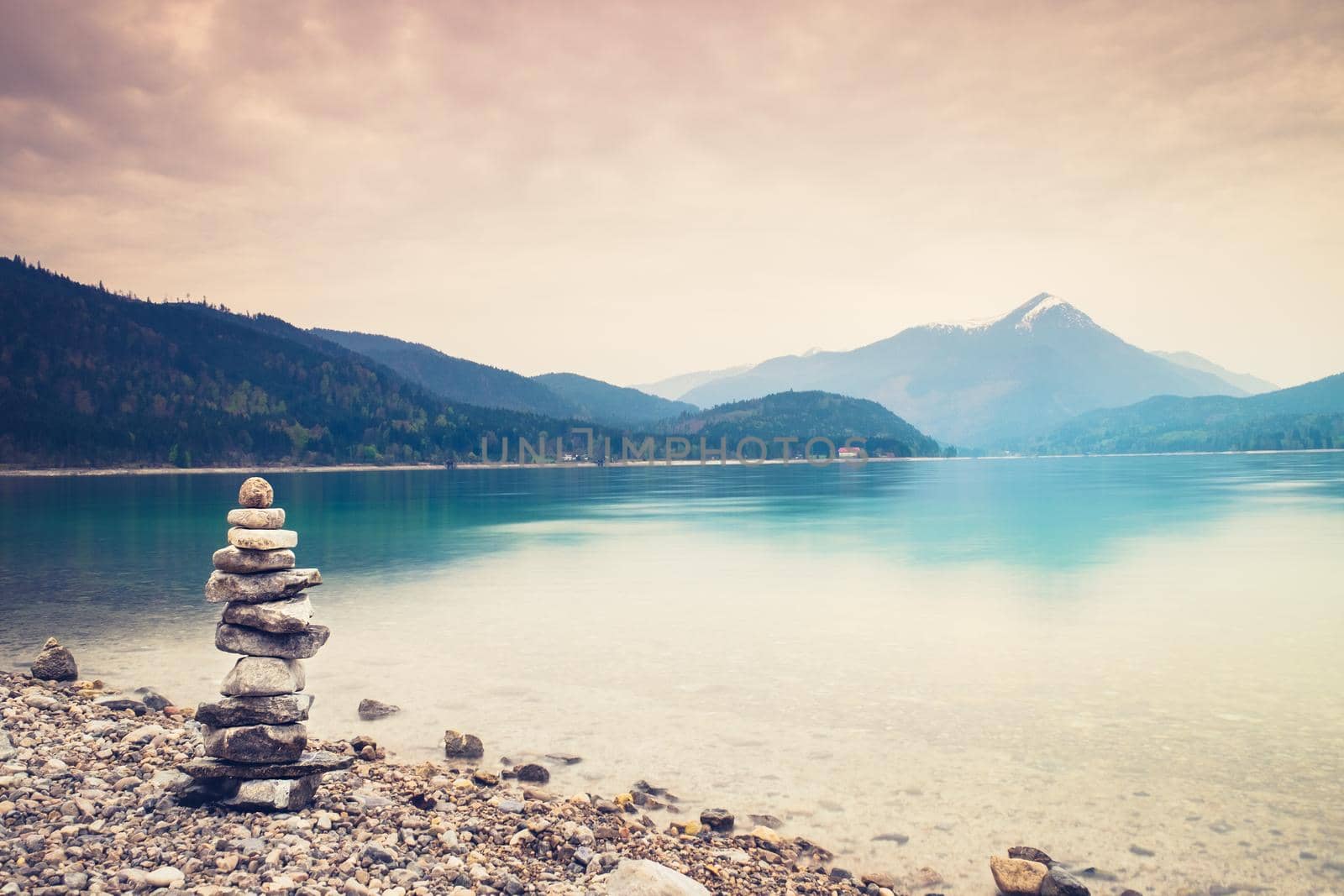 Pile of balanced pebbles on the bank of lake mirroring sky in the background. Stone stack at beach