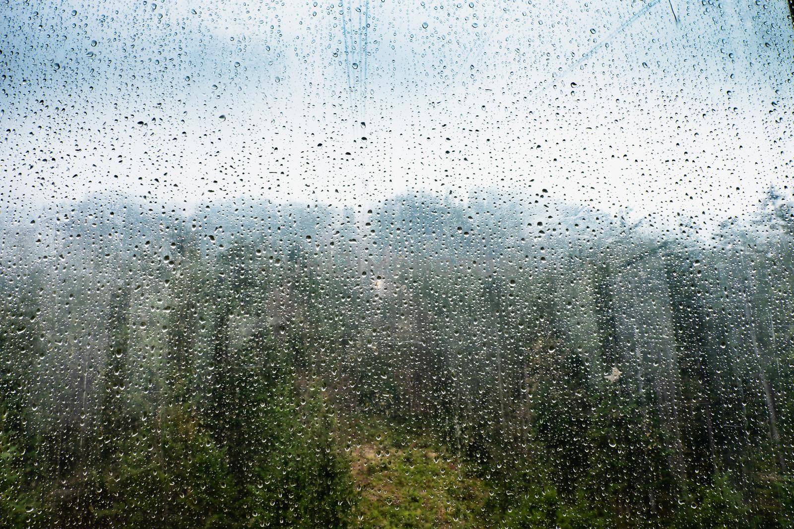 Raindrops on glass window of cableway. Sad view from overhead cable Car by rdonar2