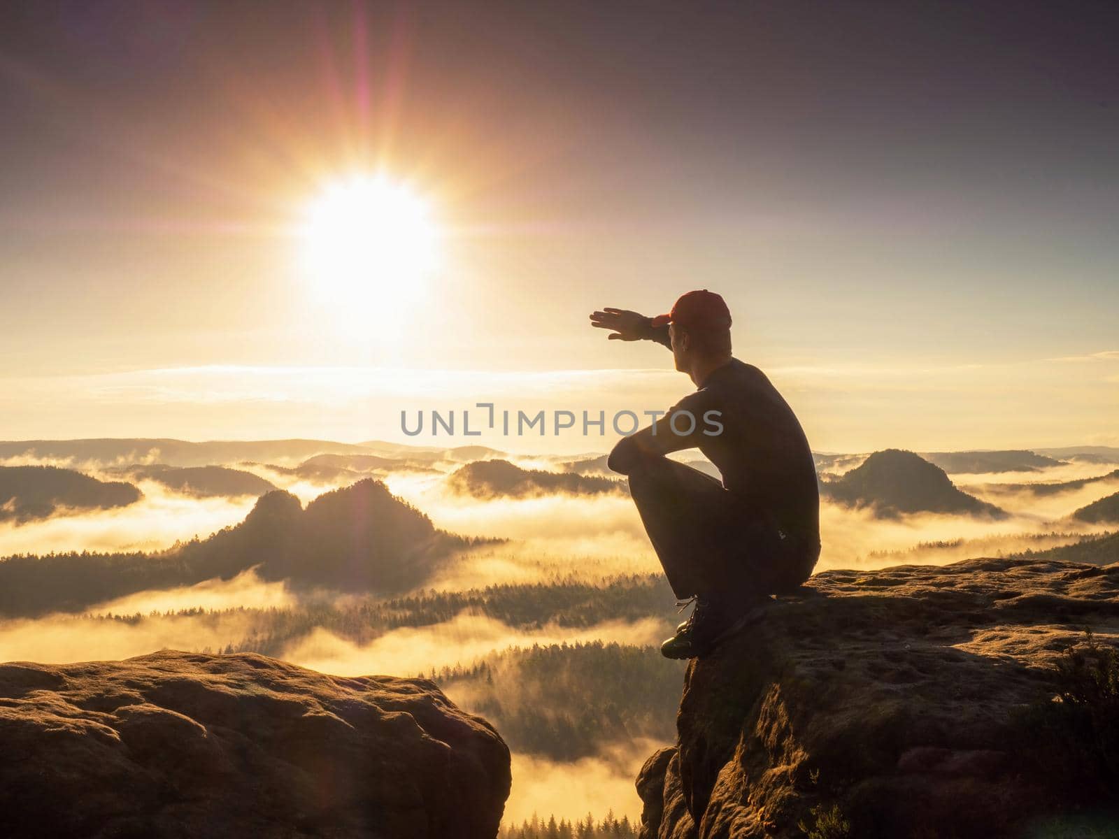 Man hiker squatting and shadowing eyes. Misty mountain valley and adventure. by rdonar2