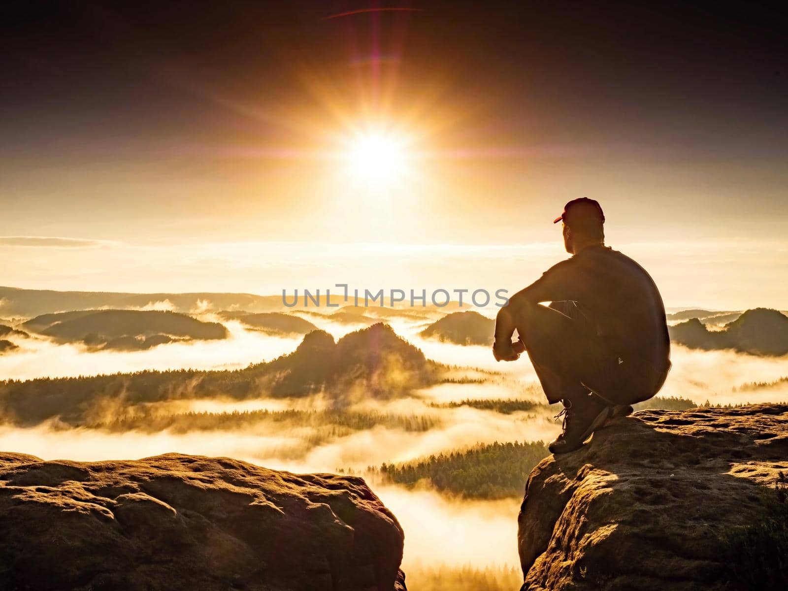 Man hiker squatting and hold knees. Hiker enjoy amazing view into mountain valley and enjoy adventure.