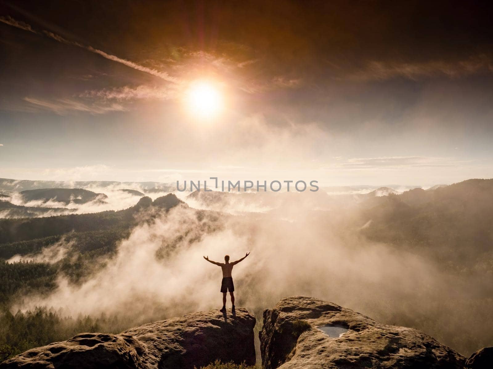 Young man on cliff edge celebrates reaching the top of the mountai by rdonar2