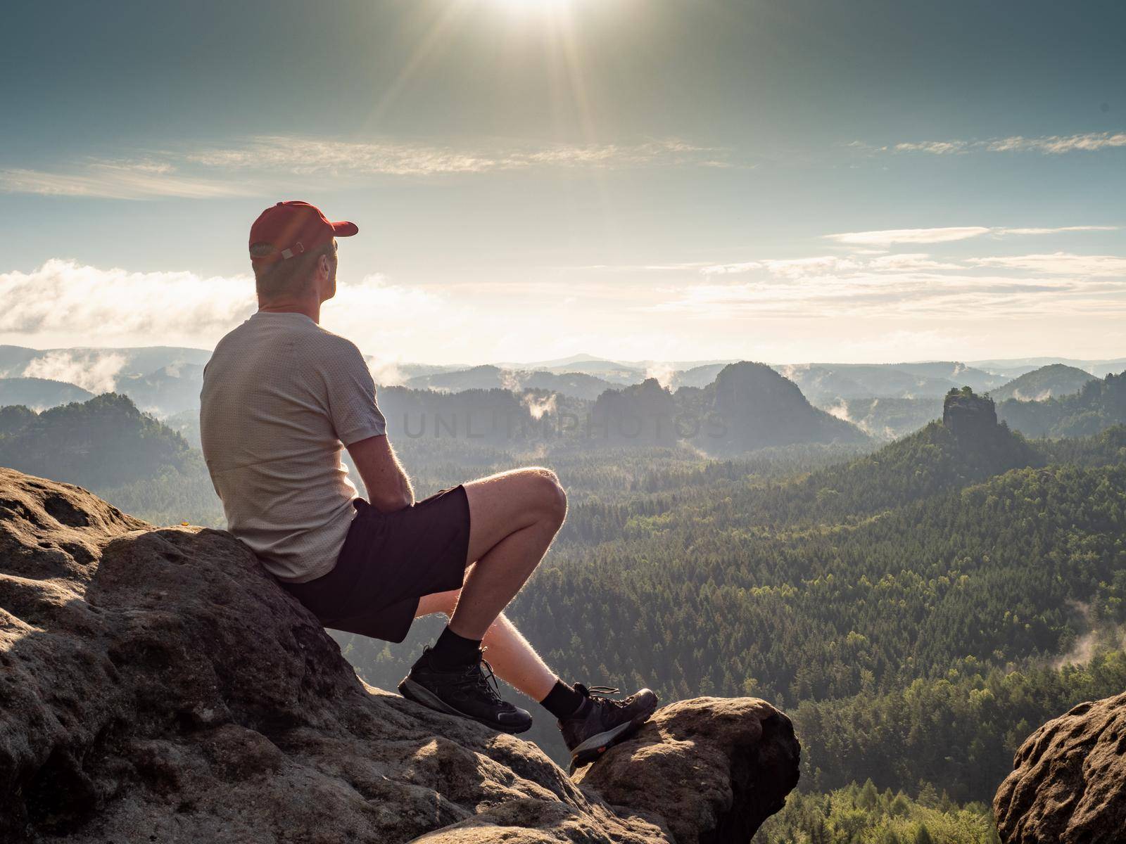 Runner man and traveler sitting on the stone at view point above landscape.