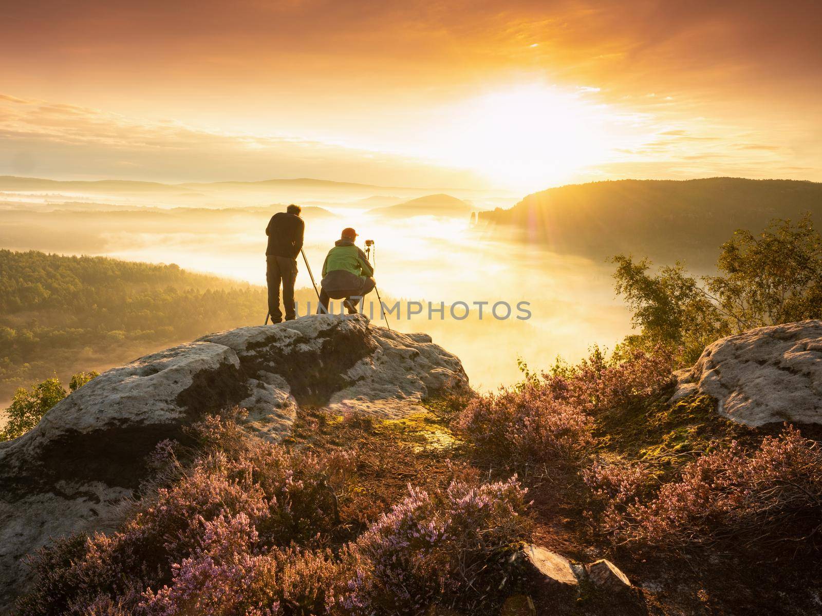 Pair of landscape photographers standing on cliff, taking photos  of misty landscape by rdonar2