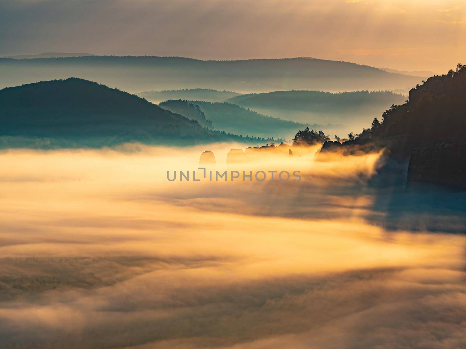 Long deep valley full of orange fall mist and Blossstock rocky pass at  horizon. Autumn morning view. Sachsische Schweiz park