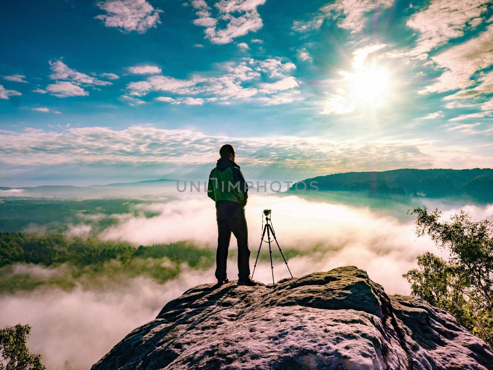 Man photographer staring into misty landscape of Saechsische Schweiz park. Beautiful morning view over sandstone cliff into deep misty valley