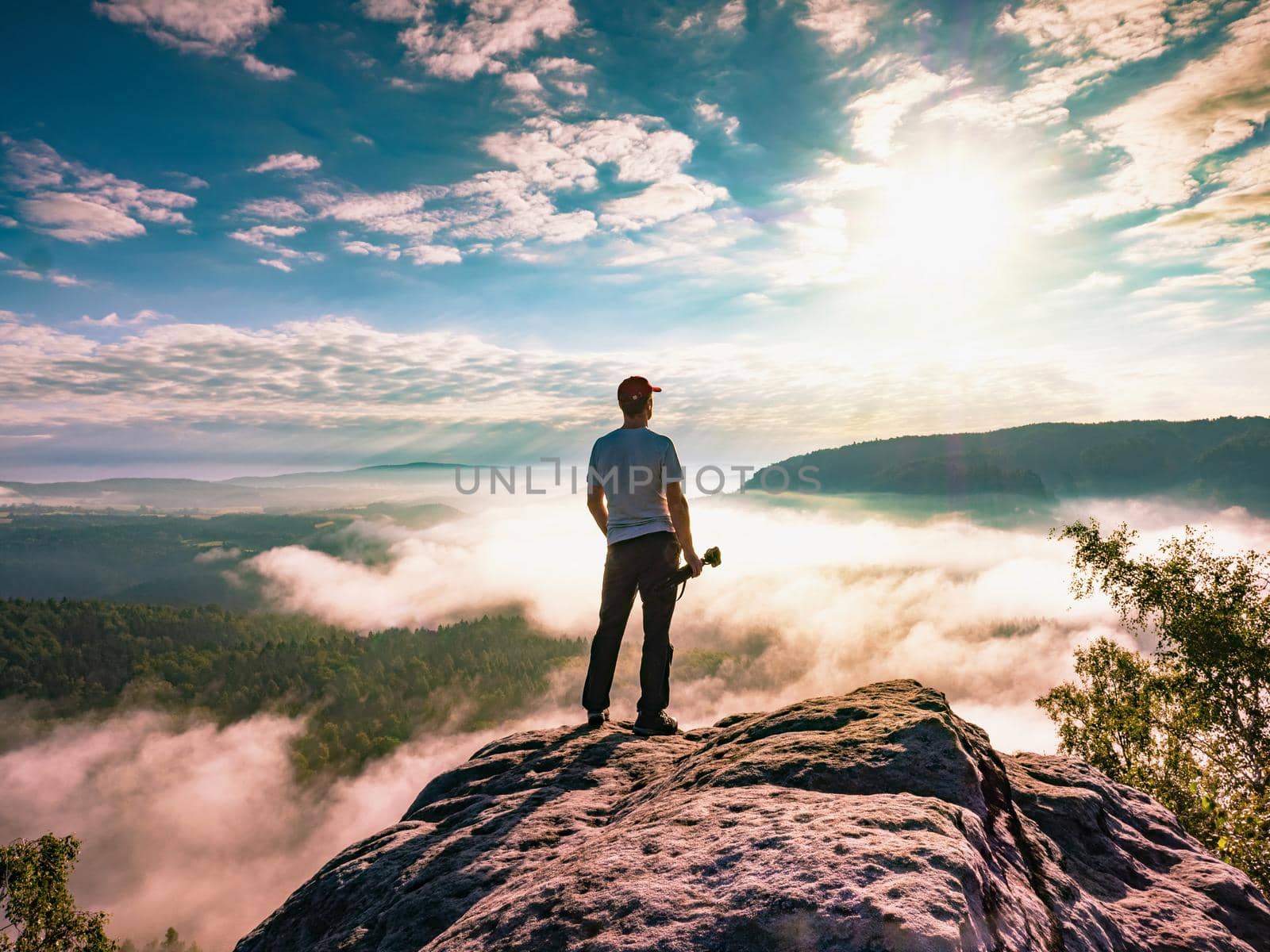 Artist with camera and tripod watch sunrise on rocky summit. The photographer enjoy misty autumn sunrise on sharp cliff in  Saxon Switzerland National Park.