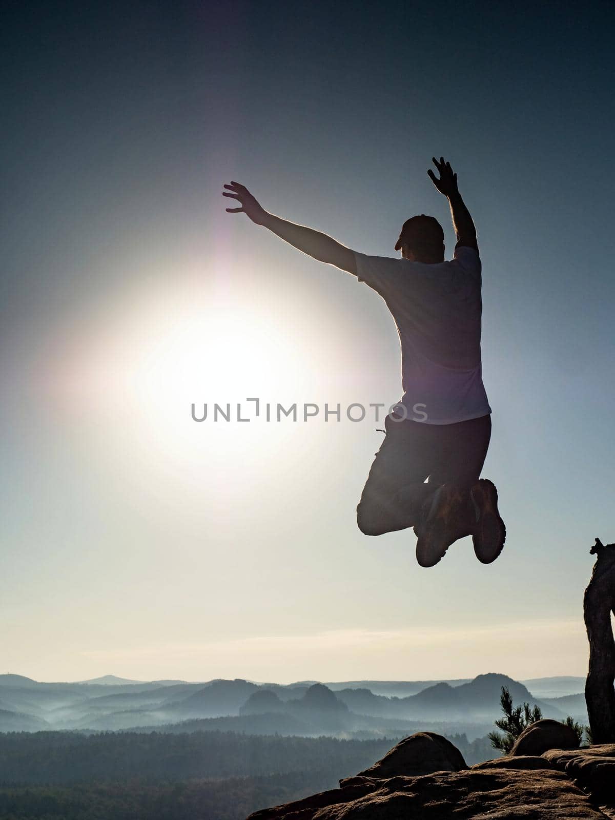 Success and freedom. The independence concept photo. Hiker jumps at the top of the mountains, with arms raised against sunrise.