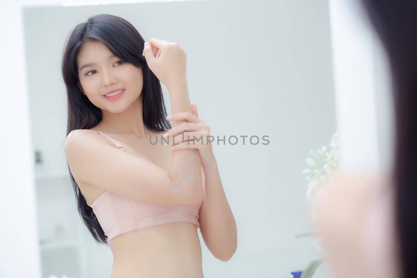 Beautiful sexy young asian woman looking mirror applying cream on arms and message, beauty girl applying body lotion skin care for health and soft hydration, treatment and cosmetic with moisturizer.