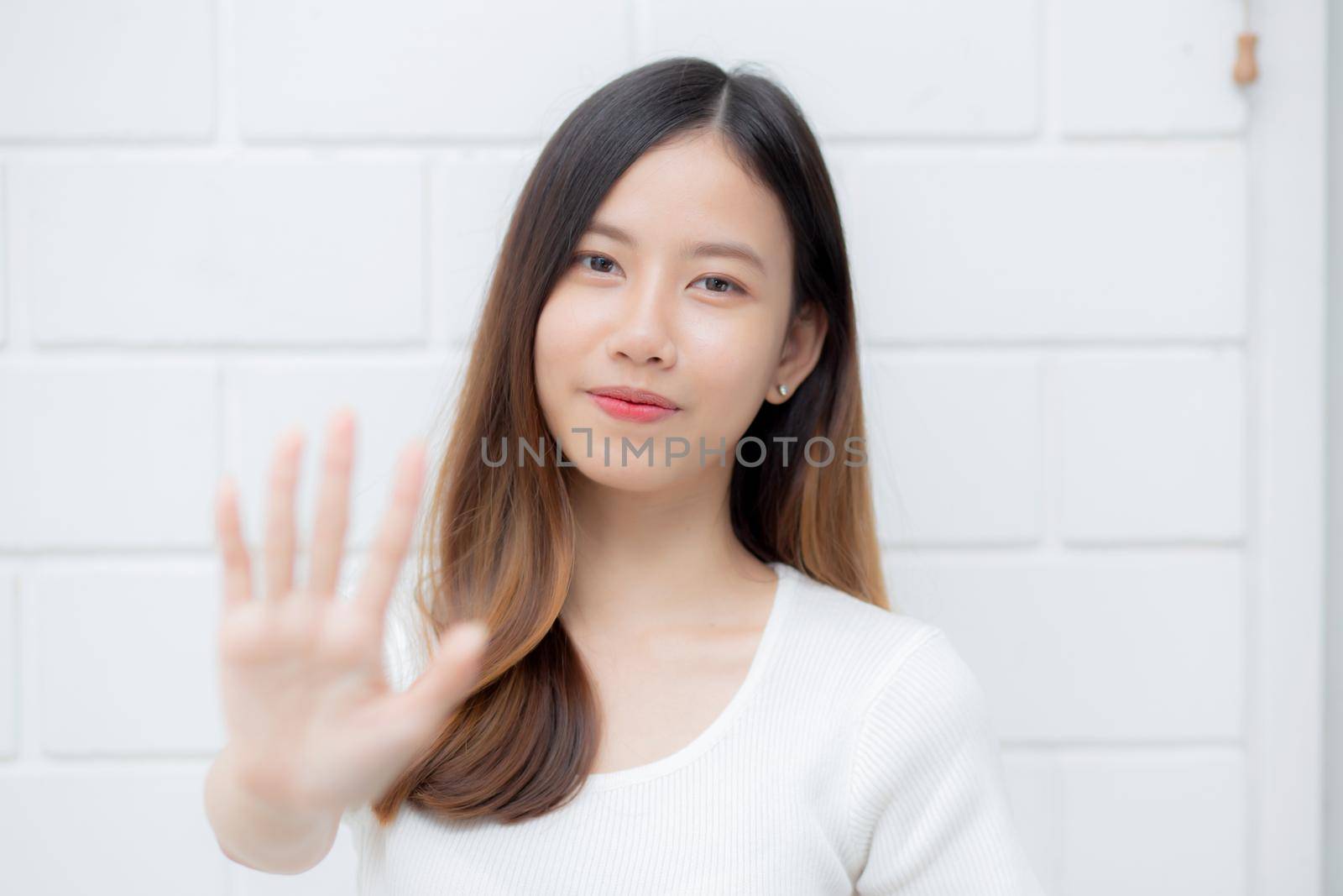 Beautiful young asian woman confident gesture say hello or greeting with waving her hand on cement background at home, friendly welcome, portrait girl cheerful expression happy and satisfied.
