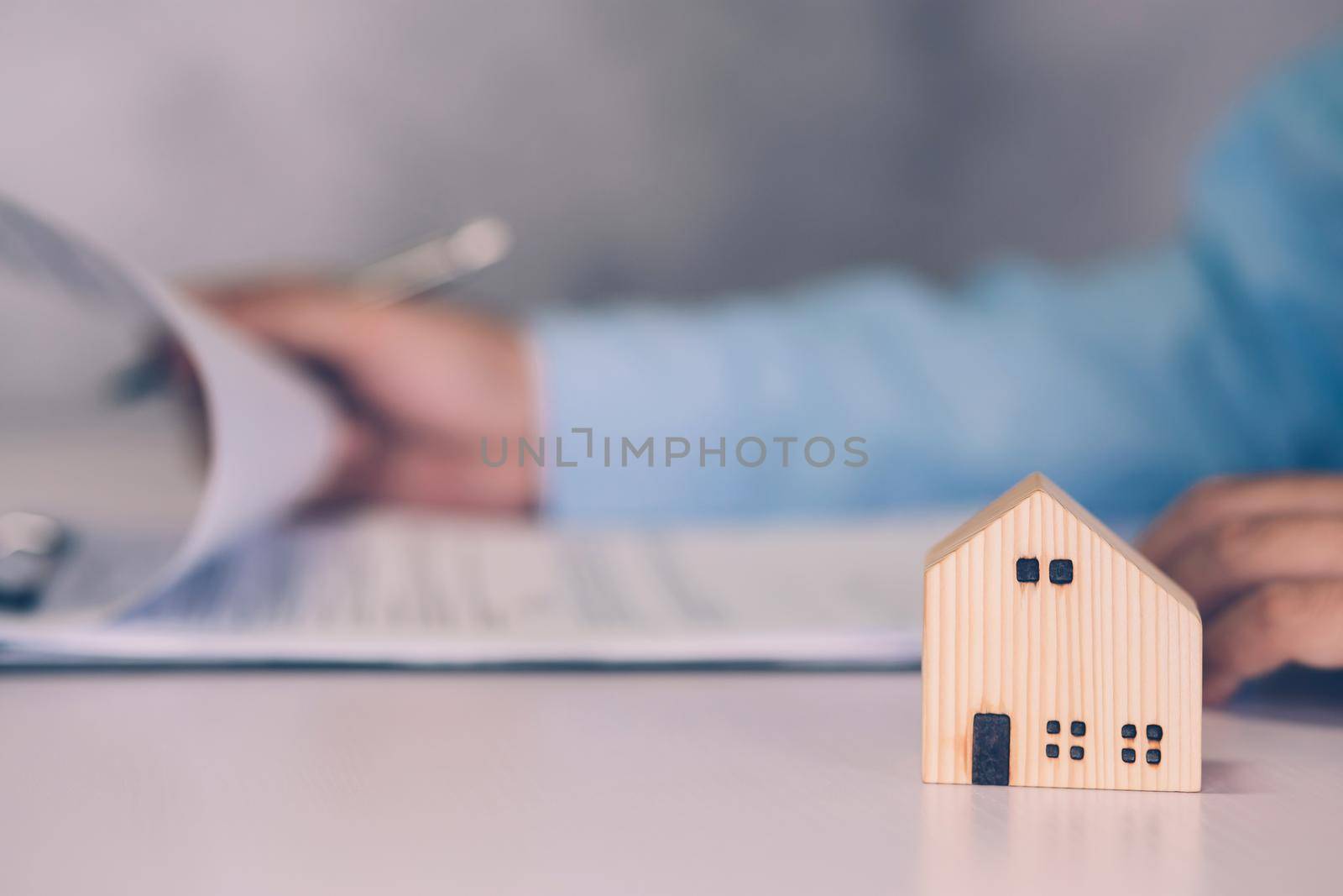 Real estate agent holding home and signing contract about agreement of real property on desk, house broker and planning investment, businessman writing on document form rent house, business concept.