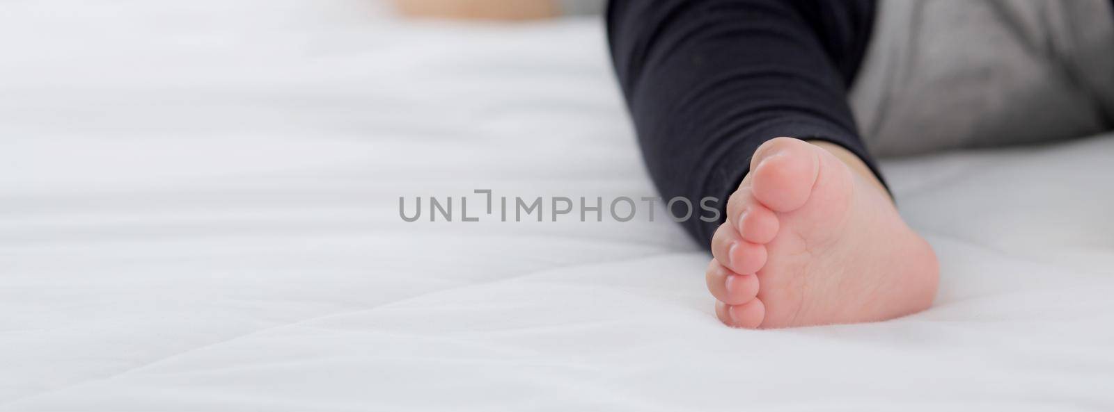 Closeup foot of asian little baby girl sleeping on bed in the bedroom at home, newborn napping with cozy and relax, infant innocence in bedtime, happy toddler cute, growth of child and emotion.