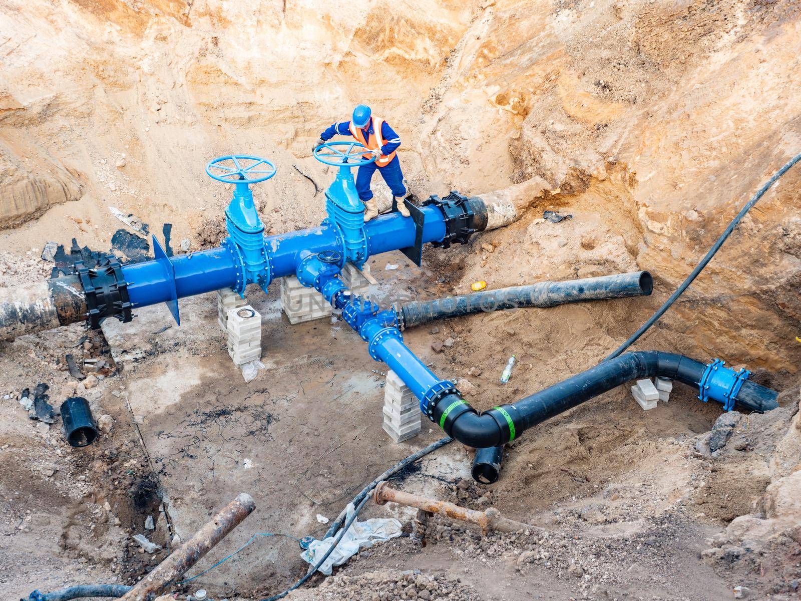 Man test valve in trench in ground with  large water pipeline of potable water delivery company