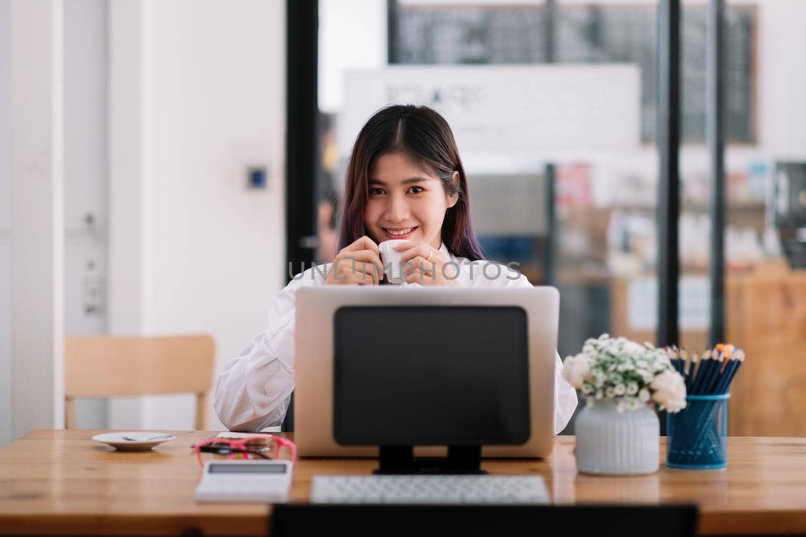 Charming asian businesswoman looking at camera and working with laptop computer in office by nateemee