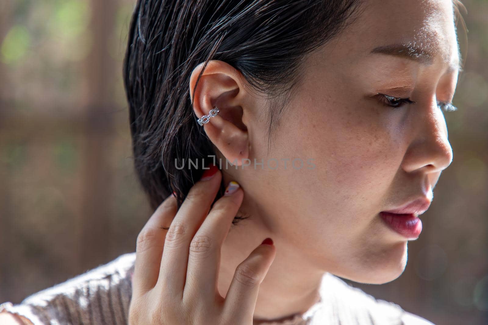 Close up portrait of a young Asian woman face and touching tips of her black short hair. Side view. Selective focus.