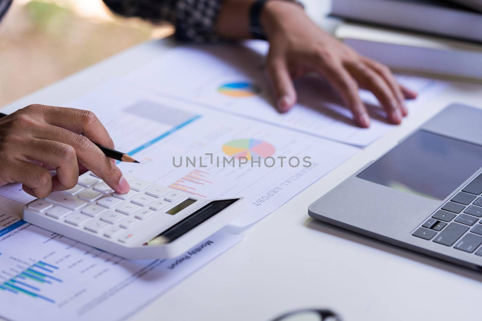 Accountant or Businessman using a calculator to calculate company financial figures from earnings papers, accounting document and laptop computer at office, business concept.