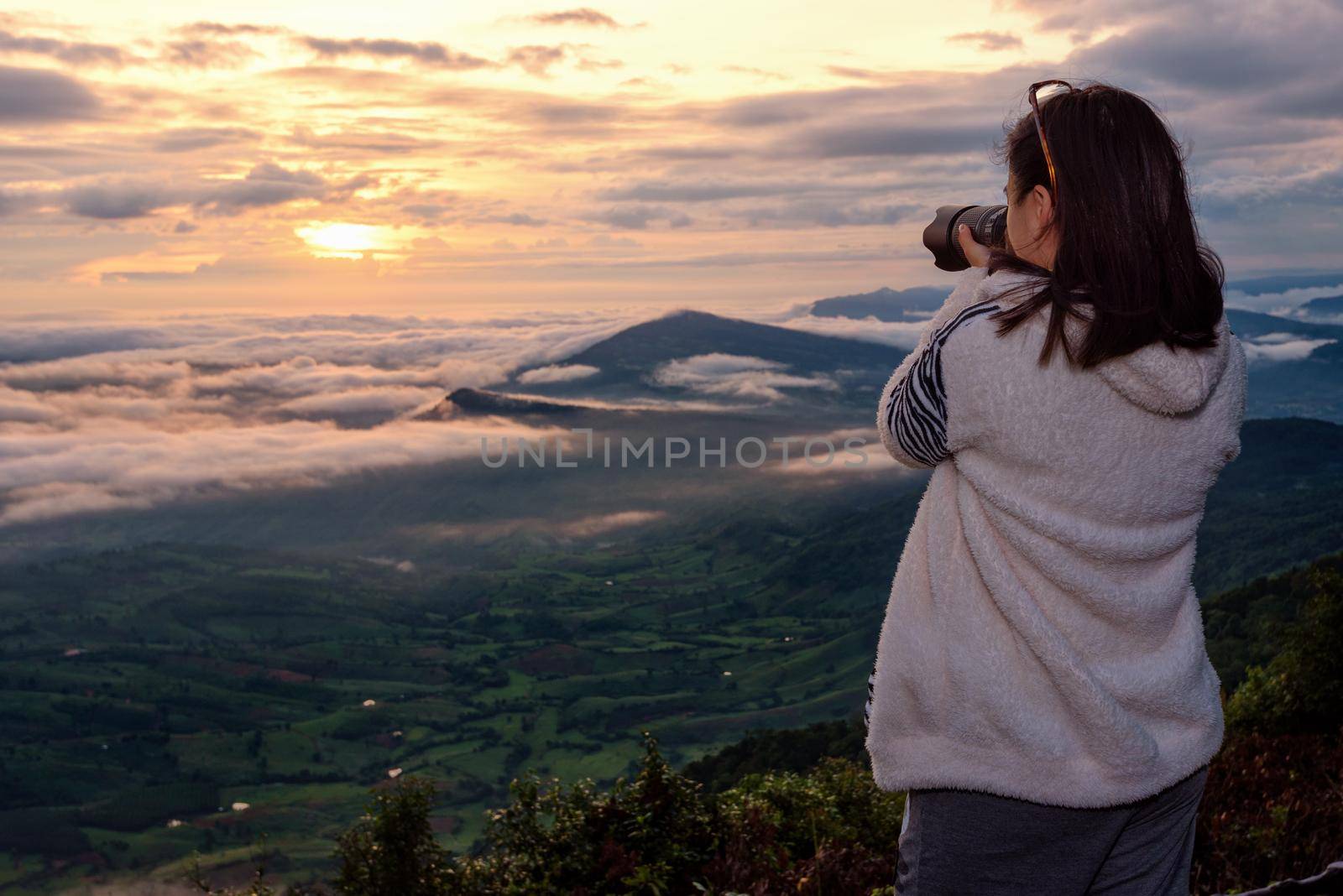 Woman tourist are using a DSLR camera photographing nature landscape the sun fog mountain in the winter during sunrise on high viewpoint at Phu Ruea National Park, Loei province, Thailand