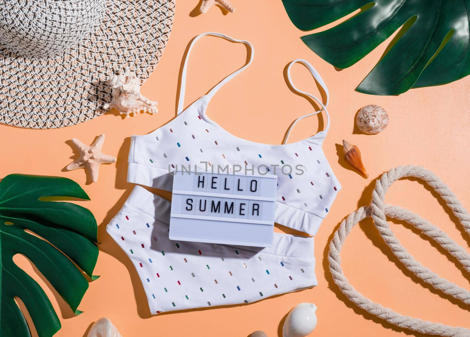 Words Hello Summer on the lightbox with swimming suit, tropical leaves and seashells by Desperada