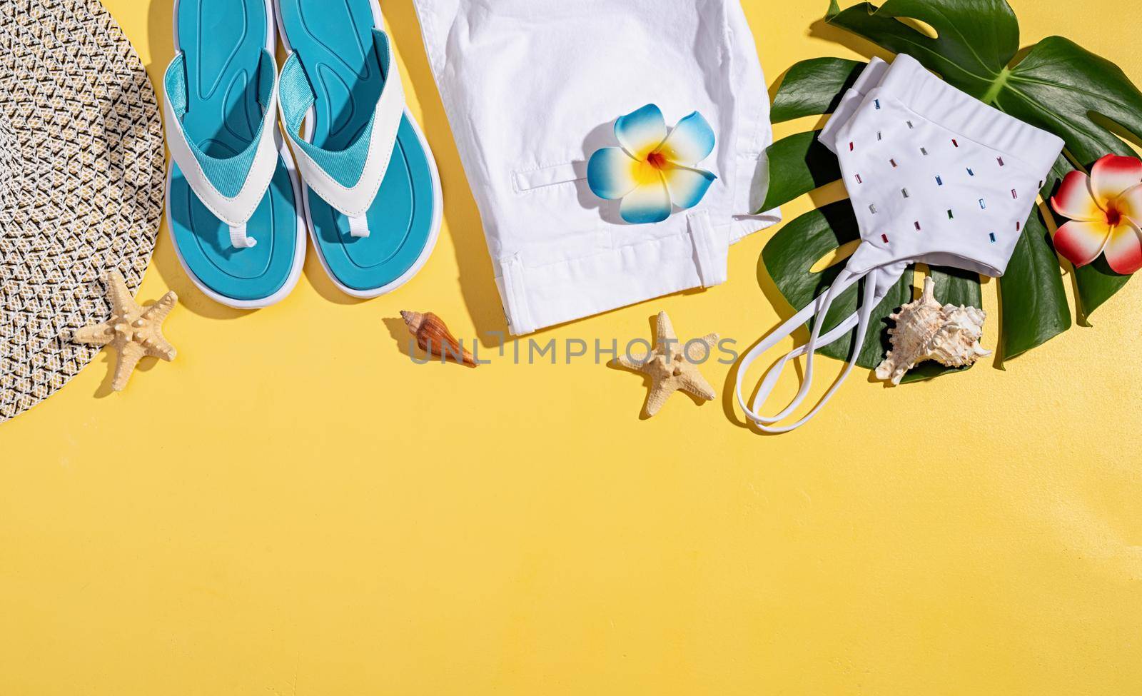 Summer and vacation concept. summer accessories with clothes, shoes, tropical leaves and flowers, flat lay on yellow background