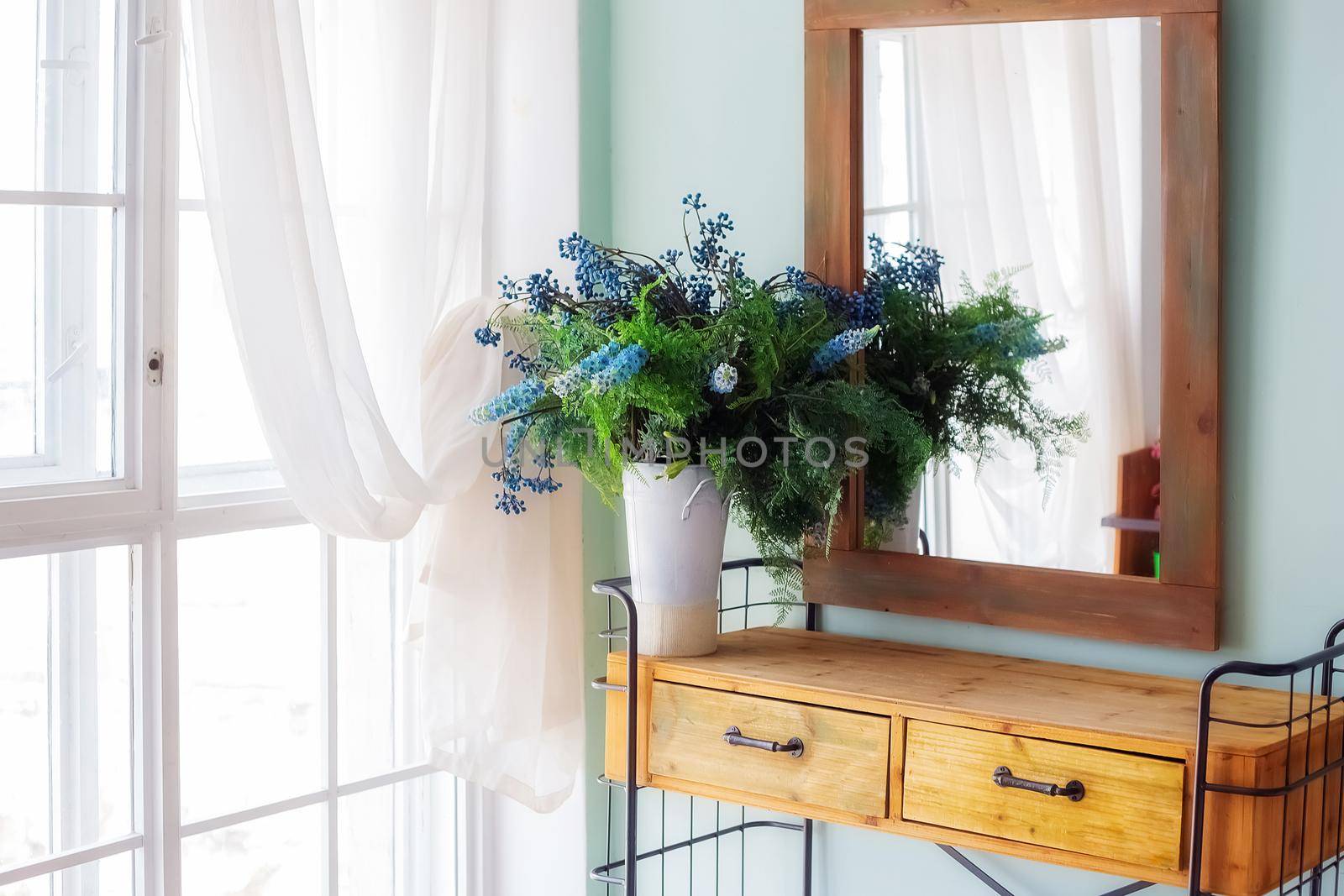 Elegant mirror in wooden frame above fancy console table with flowers  by galinasharapova