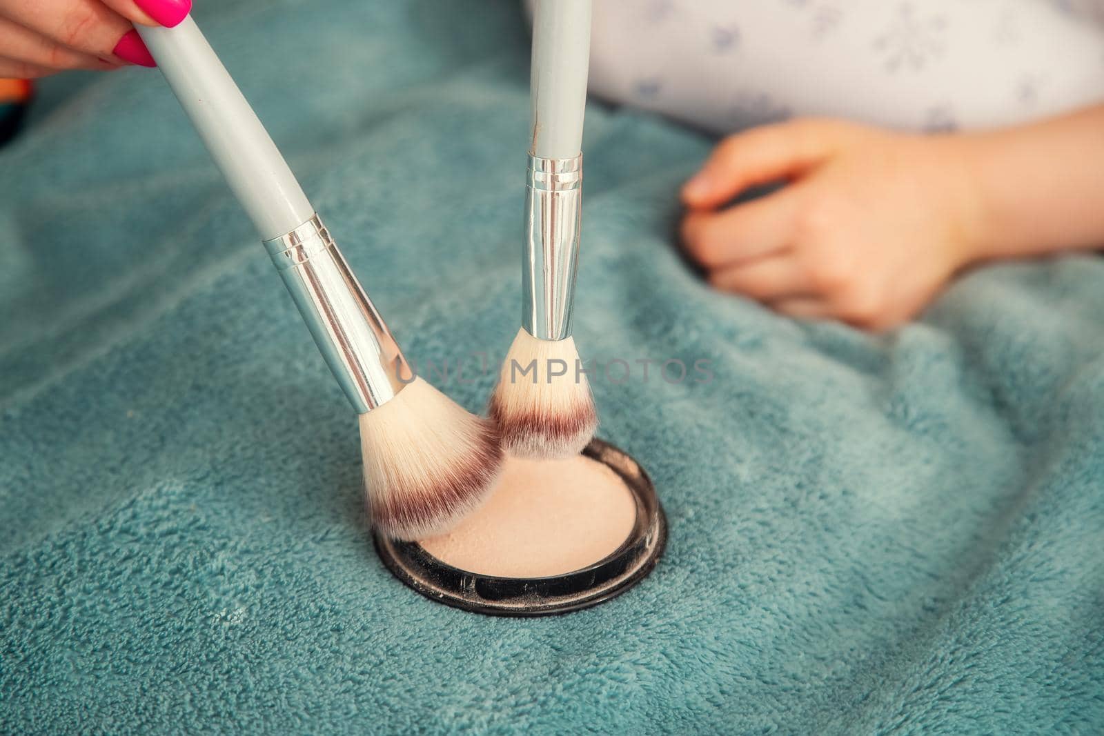 Woman hands of mom and daughter gaining compact powder on a large fluffy cosmetic brush. Close-up view with shallow depth of field