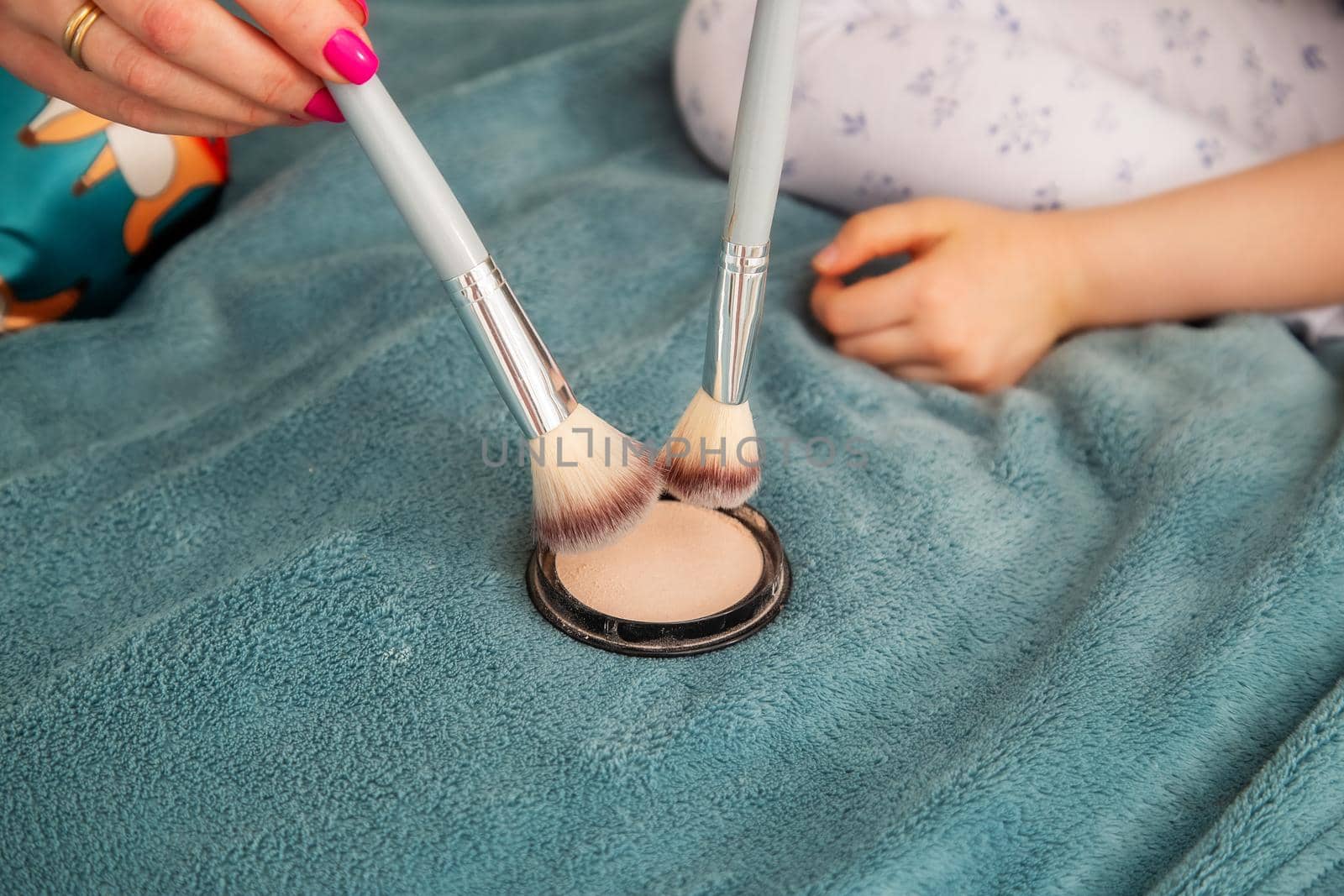Woman hands of mom and daughter gaining compact powder on a large fluffy cosmetic brush. Close-up view with shallow depth of field