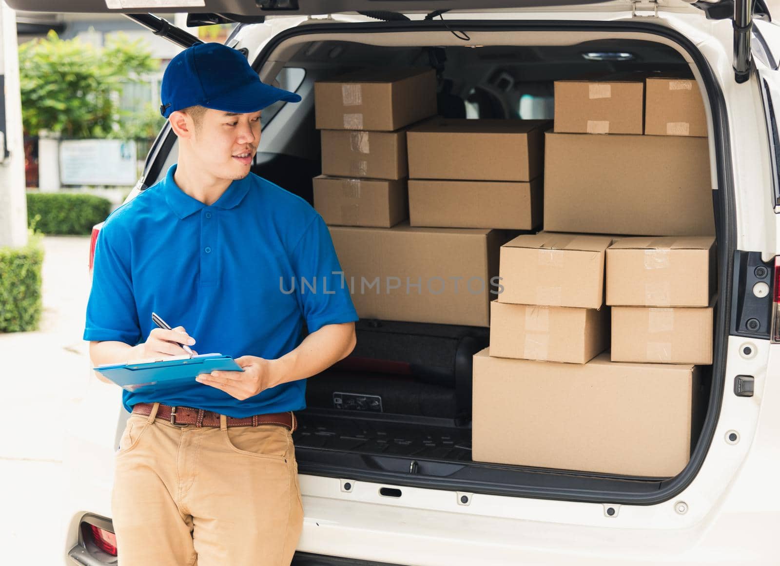Asian young delivery man courier in uniform hold documents clipboard checking list parcel post boxes near a car for service shipment to customer, Online shopping service concepts