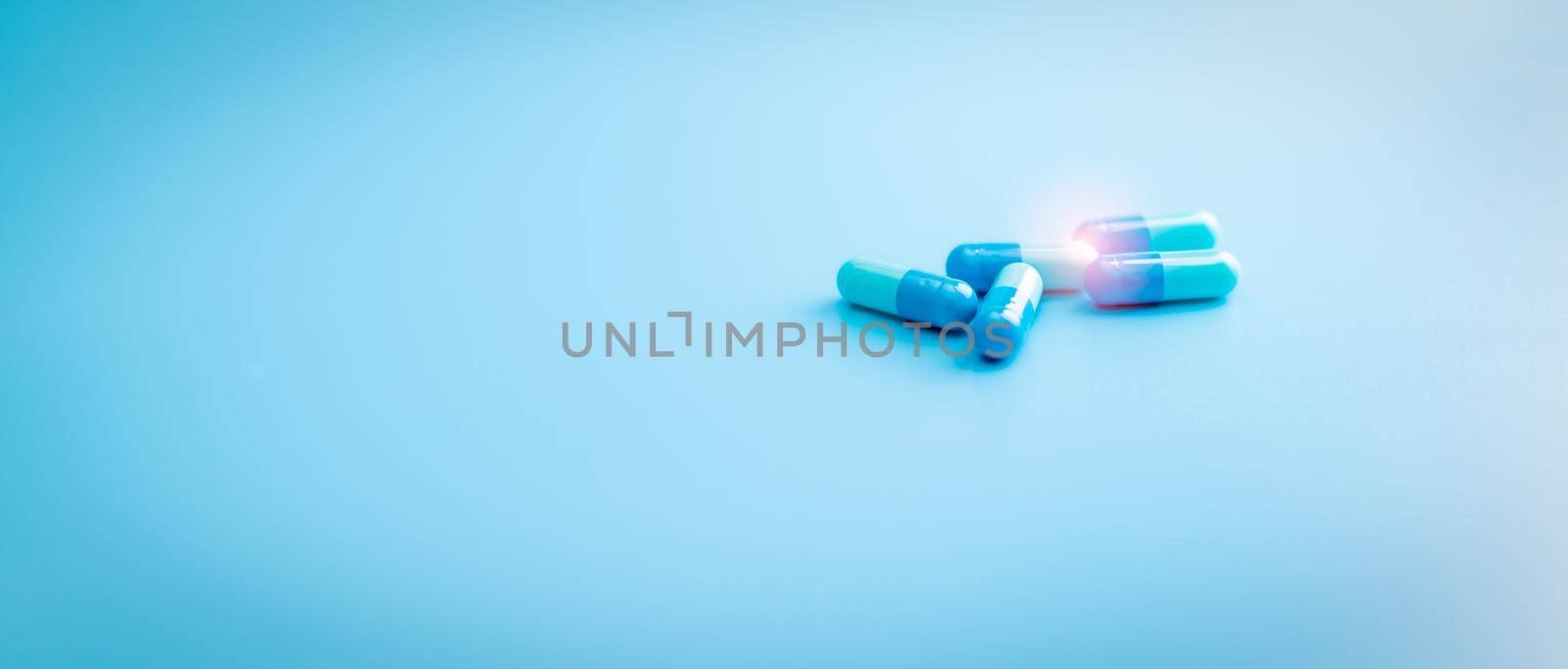 Blue capsule pills on blue background. Pharmacy shop banner. Pharmaceutical industry. Antibiotic capsule pills. Antibiotic drug resistance. Pharmaceutical industry. Prescription drugs. Drug research. by Fahroni