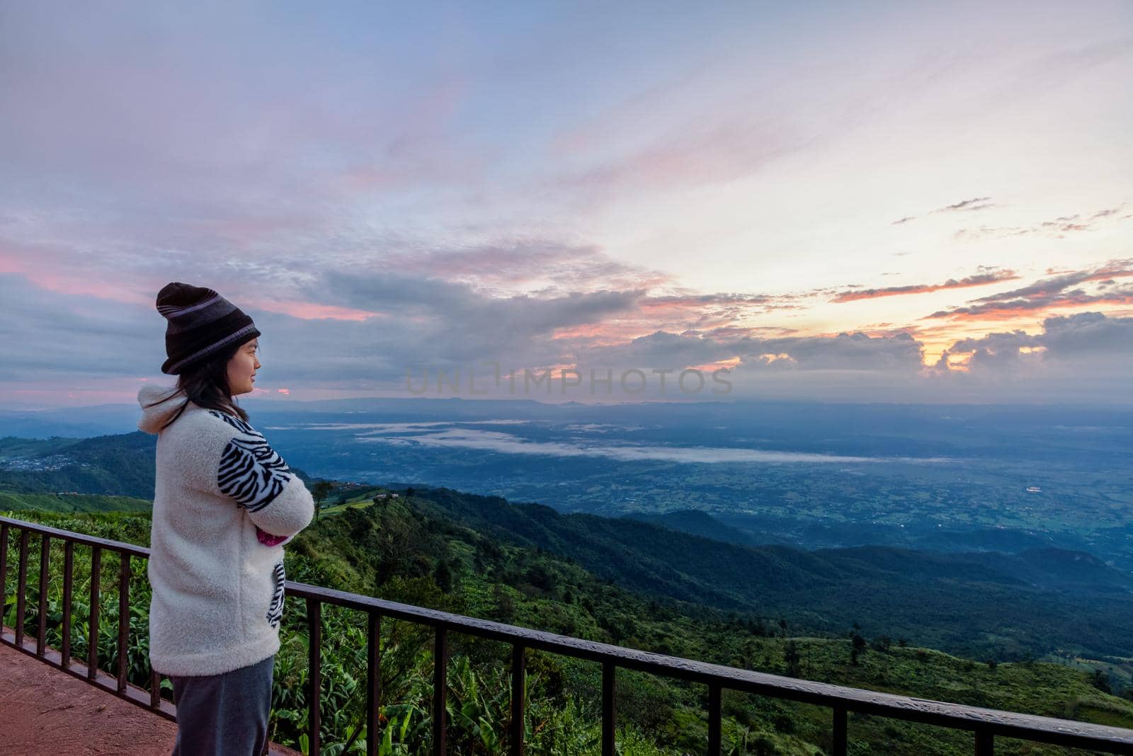 Woman tourist in a sweater dress standing watching the beautiful nature landscape of the forest and mountain during the sunrise on the high peak in the morning at Phu Thap Boek Viewpoint Phetchabun, Thailand