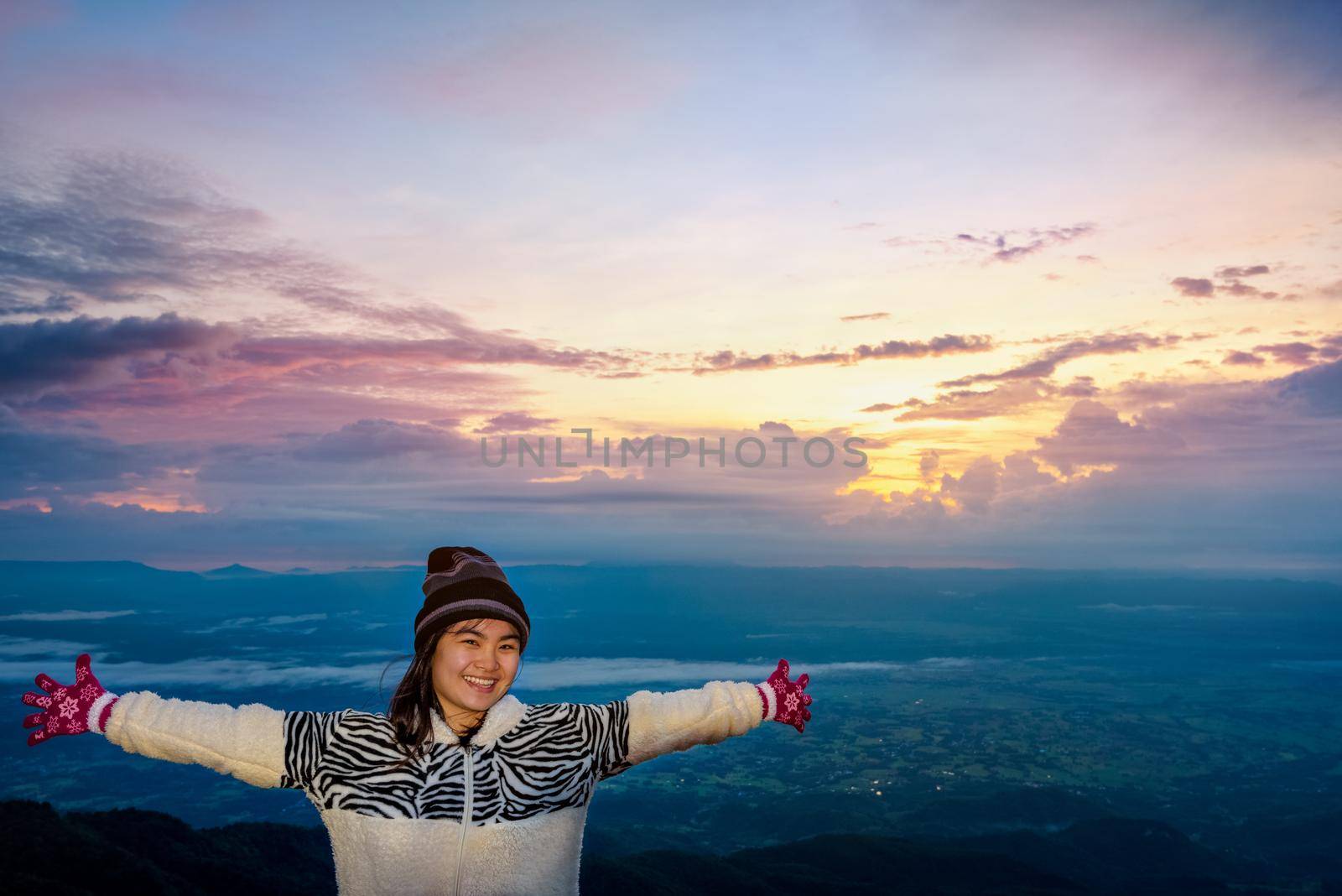Woman tourist in a sweater dress standing outstretched arms, happy while watching the beautiful nature landscape of the forest and mountain during the sunrise at Phu Thap Boek Viewpoint Phetchabun, Thailand