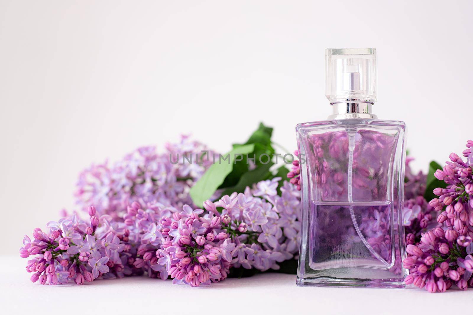 A bottle of perfume and lilac on a white background . Women's perfume. Spring fragrance. Aromatherapy. Nice smell. Beauty and fashion. Article about the choice of fragrance. An article about current flavors . copy space. A branch of lilac. Nature