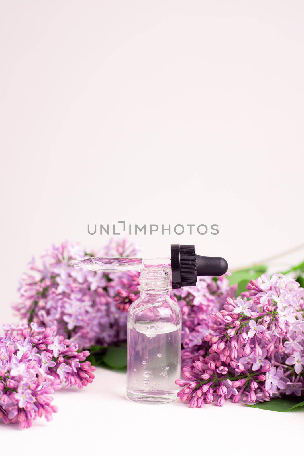 Hyaluronic acid bottle and lilac on a white background . Beauty container. Skin care. Vitamins for the skin. Rejuvenation. Female beauty. An article about the benefits of hyaluronic acid. Article about the choice of hyaluronate. Copy space. A branch of lilac. Flowering . Nature