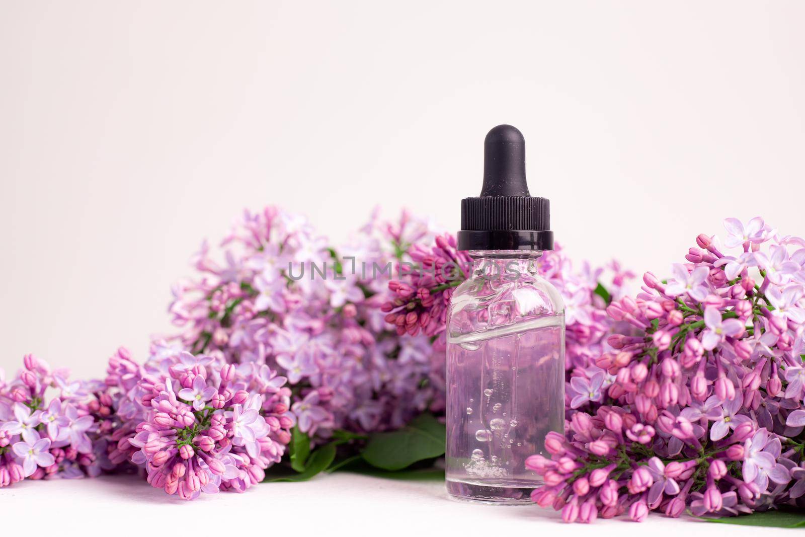Hyaluronic acid bottle and lilac on a white background . Beauty container. Skin care. Vitamins for the skin. Rejuvenation. Female beauty. An article about the benefits of hyaluronic acid. Article about the choice of hyaluronate. Copy space. A branch of lilac. Flowering . Nature