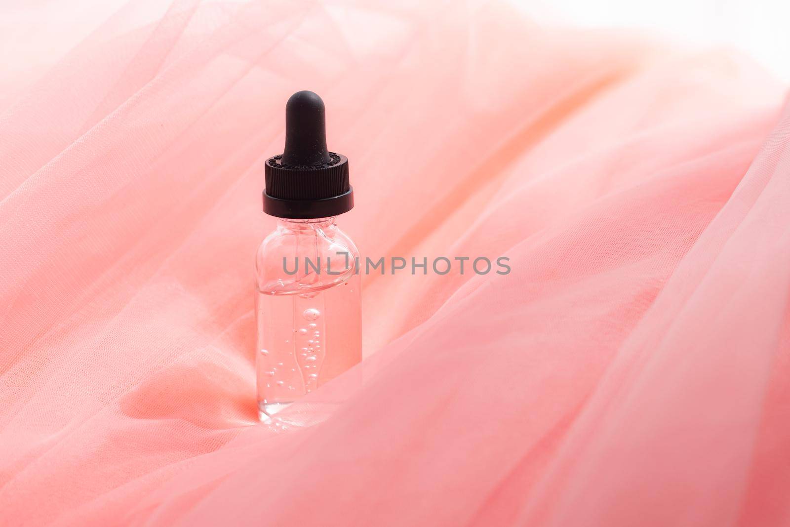 Hyaluronic acid bottle on coral fabric . Beauty container. Skin care. Vitamins for the skin. Rejuvenation. Female beauty. An article about the benefits of hyaluronic acid. Article about the choice of hyaluronate. Copy space.