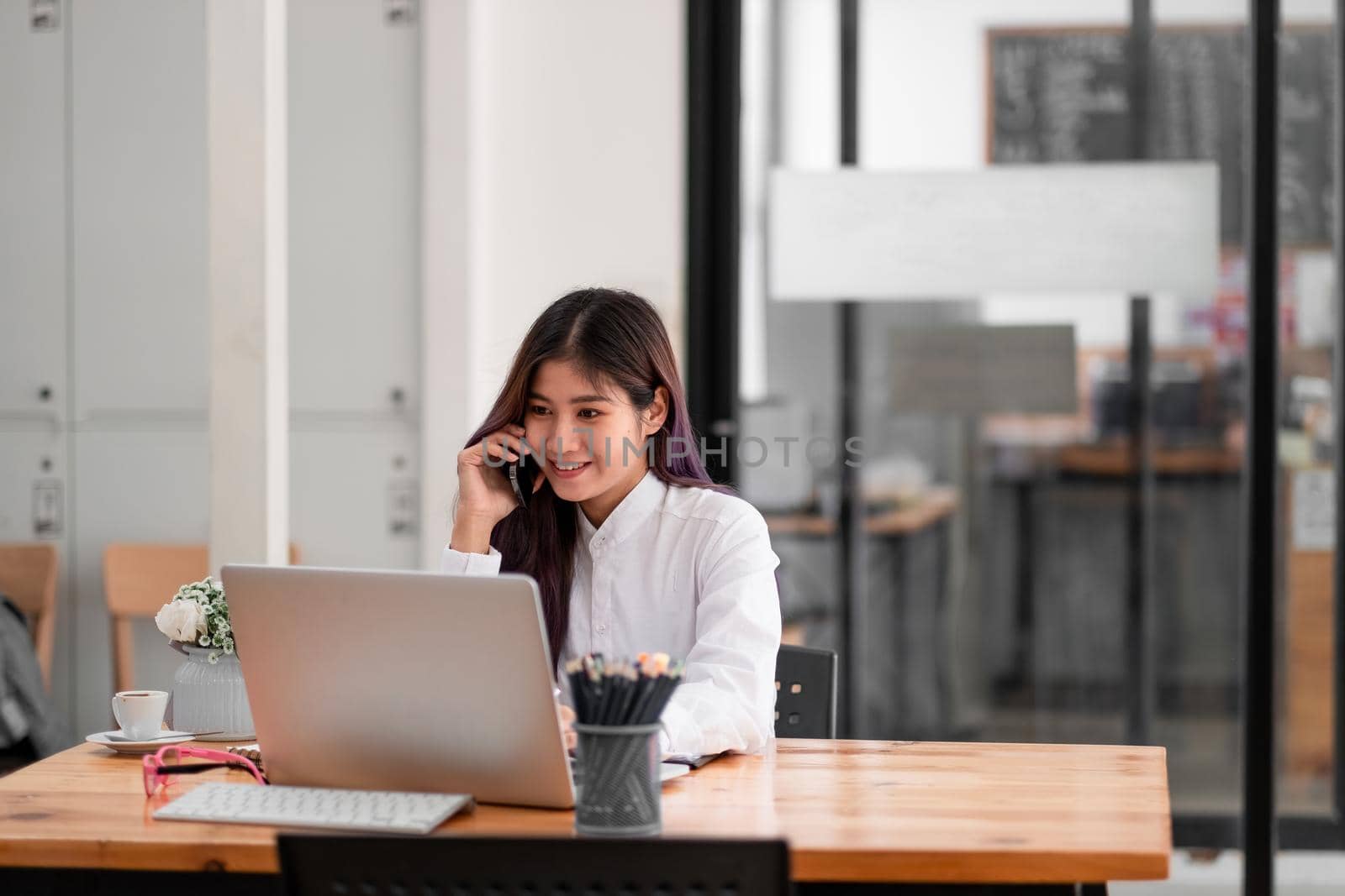 Photo of cheerful positive asian pretty woman using laptop and talking on phone